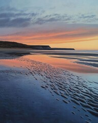 Serene sunset over a calm beach with reflective water and gentle waves.