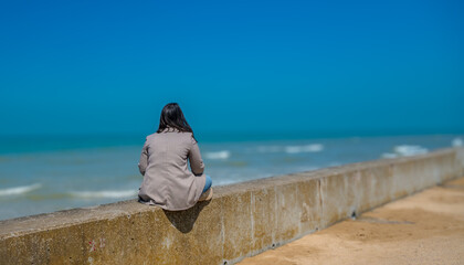 eine Person sitzt am Meer und schaut in die Ferne Symbolfoto für Zukunft, Entspannung, Einsamkeit, Perpektive, Nachdenklichkeit, Ruhe