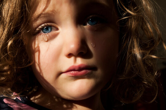 Full frame close-up portrait of a sad girl with piercing blue eyes crying