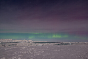 A stunning display of the aurora australis over Antarctica, with vibrant green, pink, and purple lights illuminating a serene icy landscape and scattered icebergs under a starry sky. © Oleksandr Matsibura