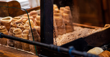Street food of Prague. Traditional national Czech sweet food. Tubes of sweet dough, cooked on an open fire. Popular dessert in Prague. Grilled food. Manufacturer trdelnik. Selective focus.