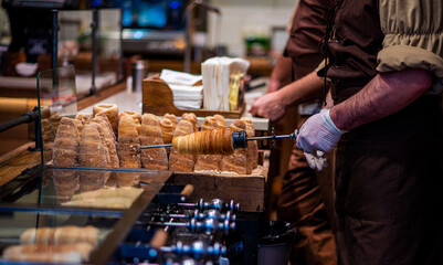 Street food of Prague. Traditional national Czech sweet food. Tubes of sweet dough, cooked on an open fire. Popular dessert in Prague. Grilled food. Manufacturer trdelnik. Selective focus.