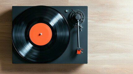 A close-up view of a black vinyl record on a turntable, featuring an orange label, atop a light wooden surface.