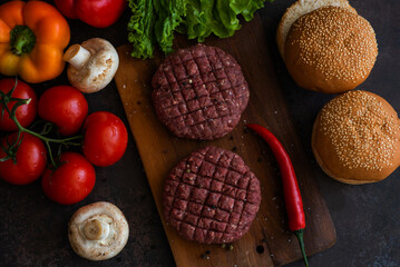 Fast food. Ingredients for making homemade fresh juicy burger. Top view and flat lay on a black table. Raw minced meat, spices, bun, lettuce and fresh vegetables.