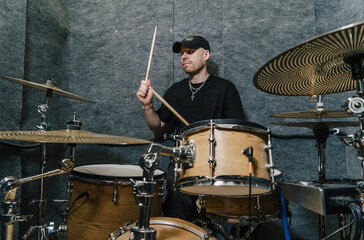 Fototapeta premium Drummer in black cap performing on wooden drum kit in soundproof music studio.