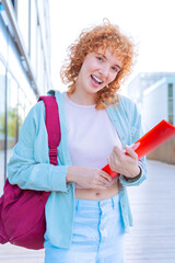 Cheerful red-haired student holding a red folder in a bright outdoor setting