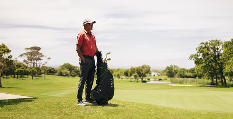 Professional golfer standing on a golf course, holding a bag of golf clubs in wide shot of golf...