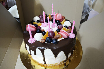 Chocolate fondant cake decorated with berries and macaroons with candles. Birthday cake