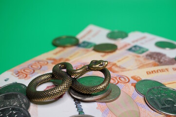A metal snake figurine and Russian rubles on a green background. Business and finance.