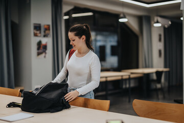 A young woman cheerfully packing her bag in a well-lit modern office. The atmosphere is...