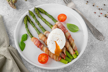 Baked green asparagus with bacon and parmesan cheese with poached egg on top on a plate. Healthy food. Top view