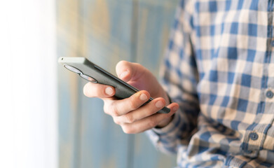 Close-up image of male hands using smartphone at night on city shopping street, searching or social...