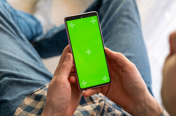 Man holding a green screen smart phone with both hand, with mock up green screen at nigh
