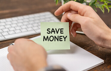 SAVE MONEY text on a sticker in hands businessman with pen and keyboard.