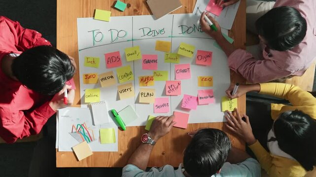 Top view of people writing and making scrum task board while writing marketing and planning strategy at colorful sticky notes. Smart team manage work performance by using kanaban board. Convocation.