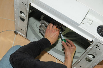 A repairman fixes a broken washing machine at home.