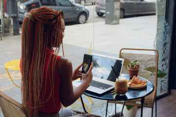 Woman in cafe scanning QR code with phone on laptop screen