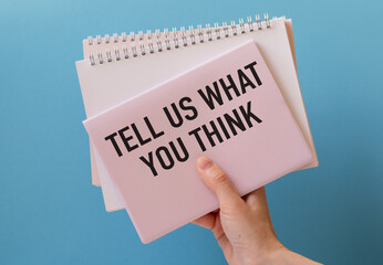 Tell Us What You Think text on a paper in hand with keyboard on blue background
