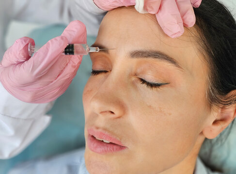 Beautiful young woman getting cosmetic injection between eyebrows, beautician making injection for glabella facial rejuvenation procedure