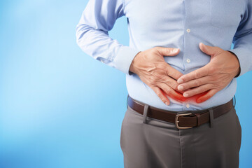 Obraz premium Man holding his stomach, indicating discomfort or pain, against a blue background.