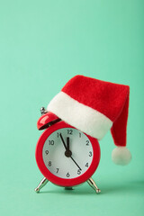 Red alarm clock with Christmas Santa hat on mint background. Vertical photo