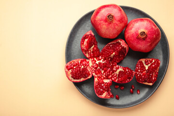 Half-cut pomegranate with seeds in plate on beige background. Top view