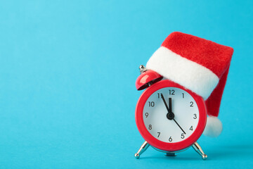 Red alarm clock with Christmas Santa hat on blue background. Top view.