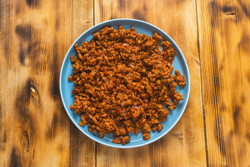 Bolognese sauce or minced beef fried with tomatoes, onions and carrots on a blue plate on a wooden table. Top view. Copyspace or space for text.