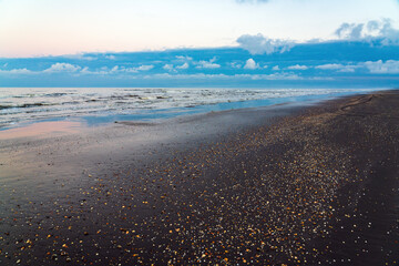 Sandy ocean shore after sunset with dark thunderclouds in the distance