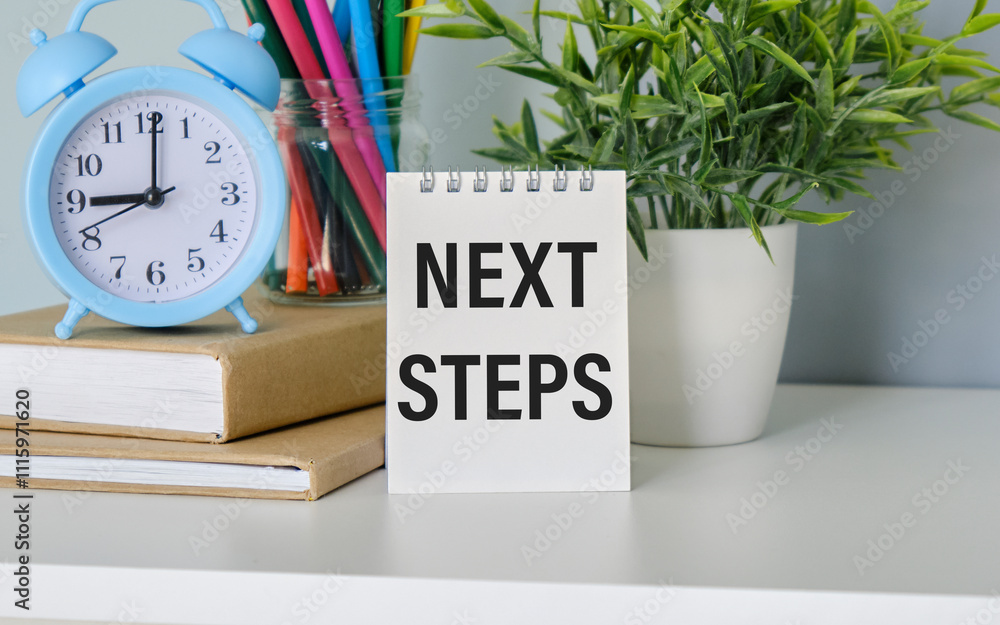 Poster the next steps are written on a notebook lying on the table next to the alarm clock and the potted f