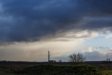 Obraz premium Cloudy skies loom over wind turbine and barren landscape in rural Nederland at dusk