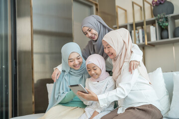 portrait of happy three different generations female muslim family enjoy holiday time together at home,sitting on couch,using tablet in living room