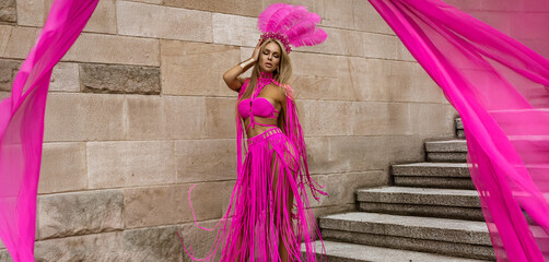 Sexy blonde model with long legs in sexy pink macrame dress sensually walks around the city.