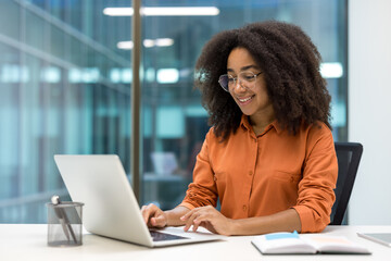 Young woman businesswoman smiling working on a laptop in a modern office . Her focus and joy...