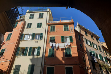 A vibrant view of colorful buildings with green shutters and white laundry hanging out to dry, capturing the essence of life in the picturesque village of Riomaggiore, Cinque Terre.