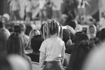 Niña de espaldas en el público de un espectáculo familiar en blanco y negro