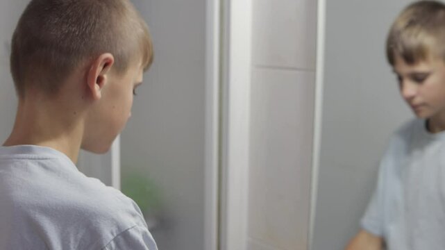 Teenage boy wipes his face with a towel in the bathroom after washing. Looking in the mirror, he engages in his morning hygiene routine, promoting freshness and cleanliness
