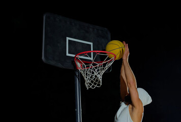 A man performs a slam dunk on a basketball court at night under the glare of bright outdoor lights