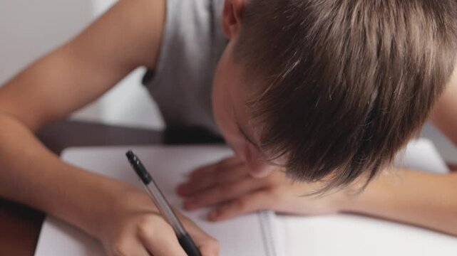 Young boy practicing cursive handwriting showcases diligence and focus while carefully forming letters on lined paper, enhancing skills in penmanship and literacy development