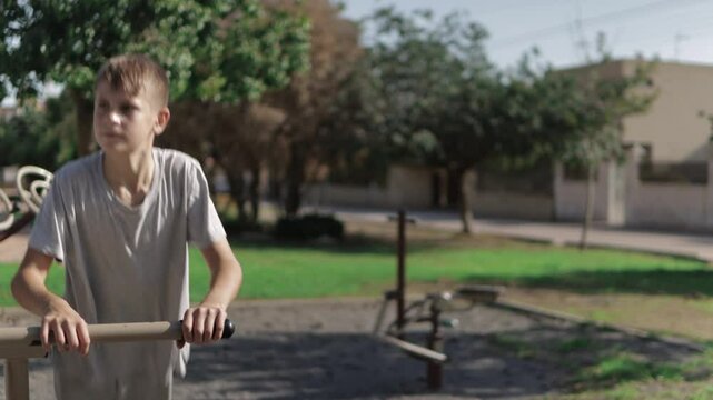 Young Boy is exercising outdoors. He is using the parallel bars at a calisthenics park. He is pushing himself up and down