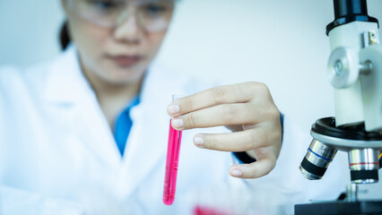 A woman in a lab coat holding a test tube with a pink liquid in it. Concept of scientific curiosity and experimentation