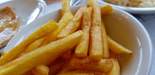 A white plate that is topped generously with french fries on a table