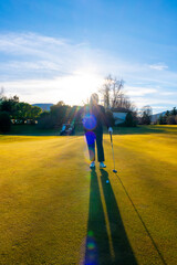 Golfer with Sunbeam and Lens Flare Standing on a Putting Green on Golf Course in a Sunny Day in Switzerland.