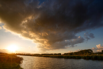 Captivating sunset over tranquil river in the Netherlands showcased by dramatic clouds and golden...