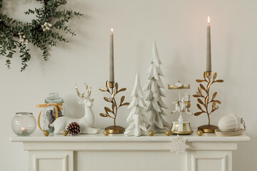 Festive mantel decorated with white reindeer figurines, gold candleholders, and seasonal greenery....