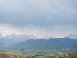 Drone view of the mountains in cloudy weather. Large dark clouds in the sky. Green and yellow grass in a field on the hills.