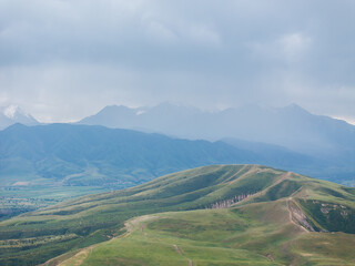 Fototapeta premium Drone view of the mountains in cloudy weather. Large dark clouds in the sky. Green and yellow grass in a field on the hills.