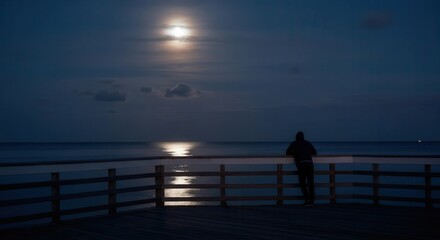 Fototapeta premium Serene moonlit pier with solitary figure gazing at sea