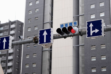 traffic light showing red signal against overcast blue sky in Tokyo, Japan. The text on the sign is...