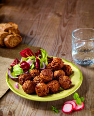 Hackbaellchen und Salat auf gruenem Telller mit Wasserglas auf rusitkalem Fond und Brot